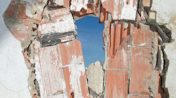 A damaged brick wall revealing a hole with a clear blue sky visible through it.